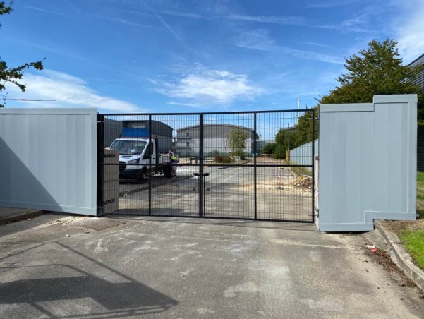 Access control vehicle gate on a construction site. Beyond the gate is a construction site and a bright blue sky.