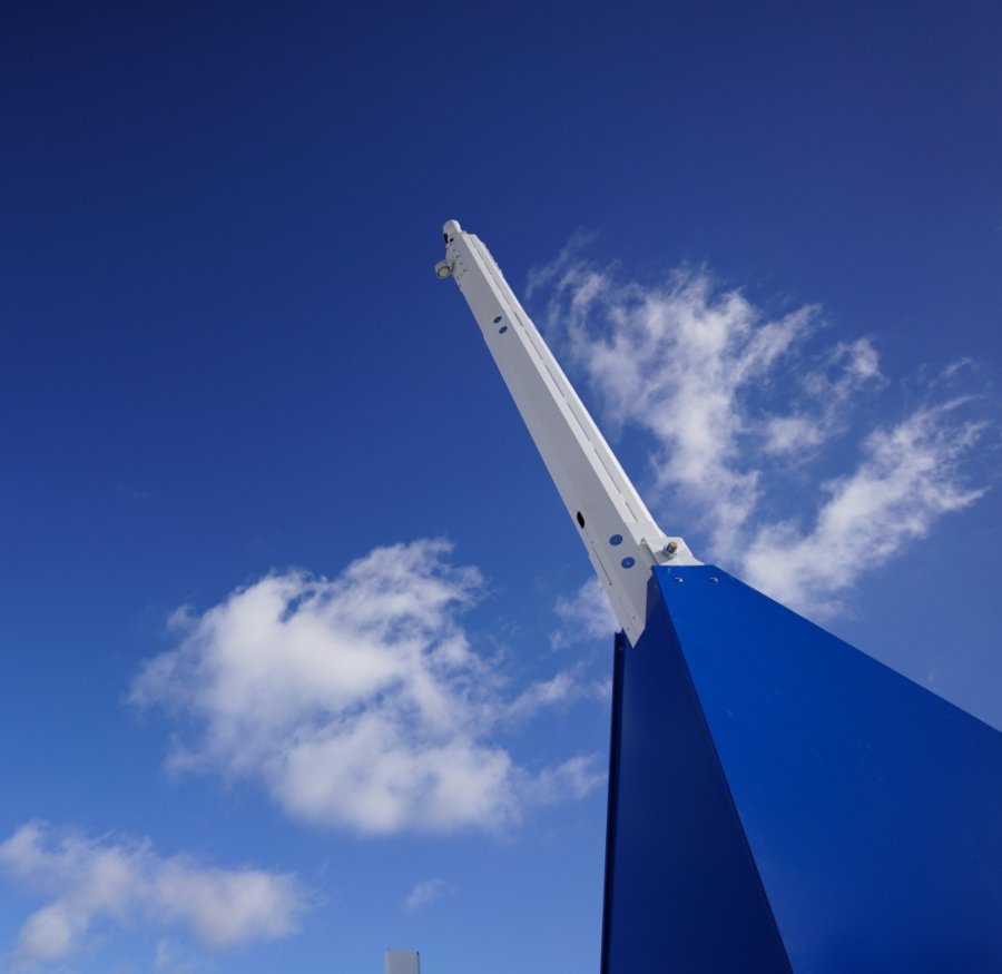 A low-angle shot of a white CCTV mast extending upwards from a blue base against a vibrant blue sky with scattered white clouds.